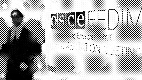 A man in a suit walks next to a roll-up banner for the OSCE Economic and Environmental Dimension Implementation Meeting (EEDIM)